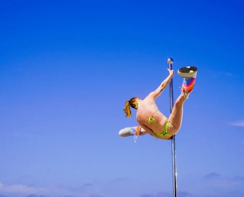 Photographer shoots pole dancer doing splits on an all star stages portable dance pole on the beach CU-2