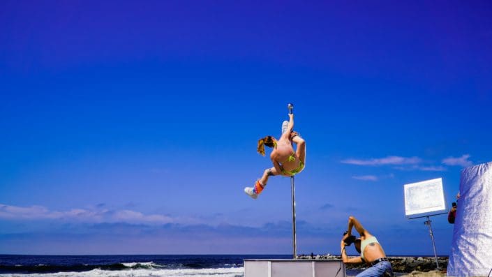 Photographer shoots pole dancer doing splits on an all star stages portable dance pole on the beach CU 4-2