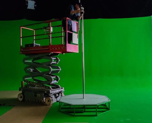 man fixes green screen portable stripper pole on a scissor lift on green screen set