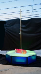 All Star Stages X Brass 45mm spinning dance pole daytime glowing green and blue with a pink skateboard on its side