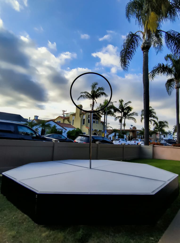 10x10x1 octo acrylic stage with spinning Lyra hoop on the grass looking thru a palm tree in the sky